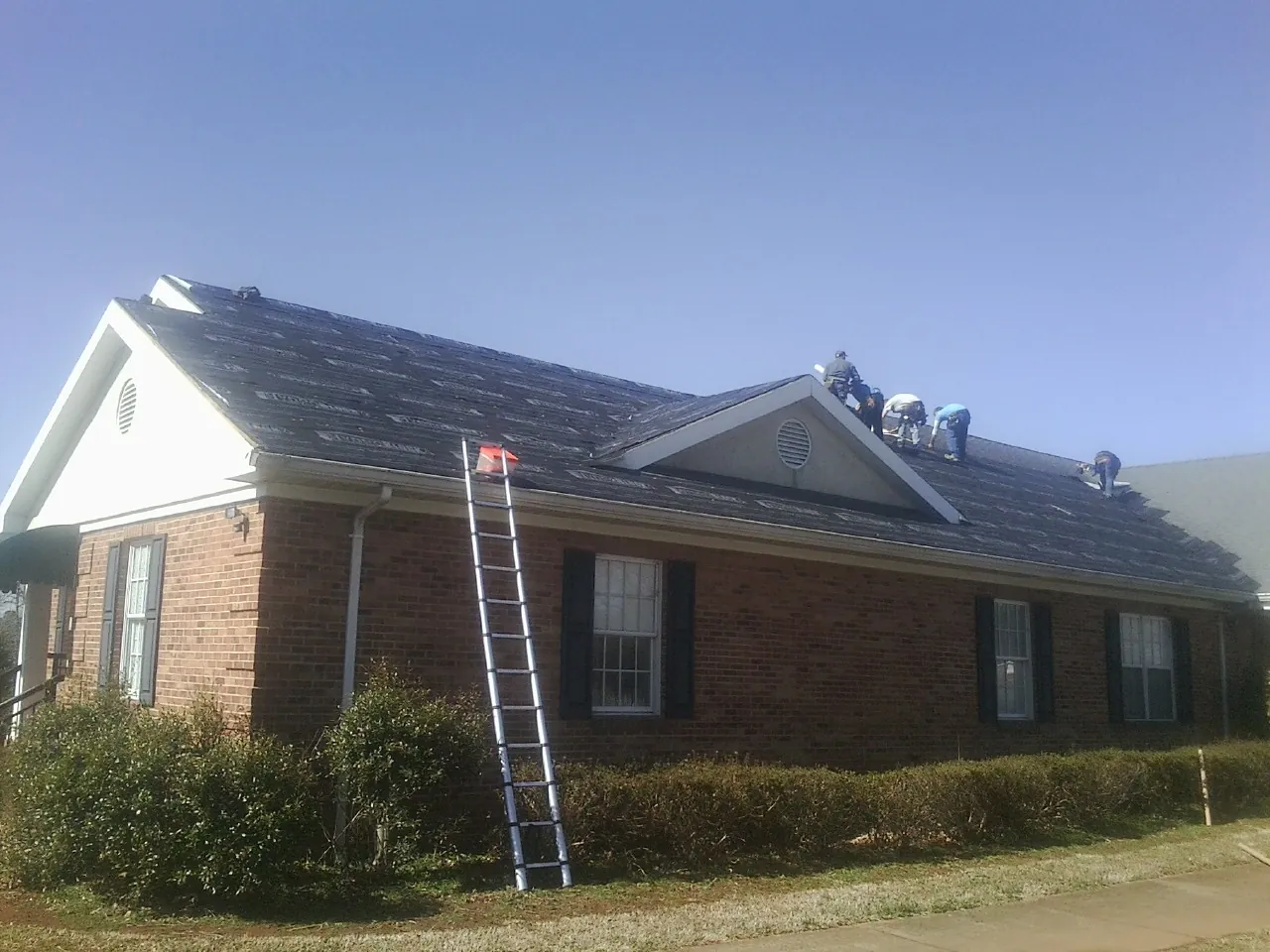 Crew tearing shingles off a brick ranch roof with a ladder set — Metal Roof Repair work by our crew in French Gulch