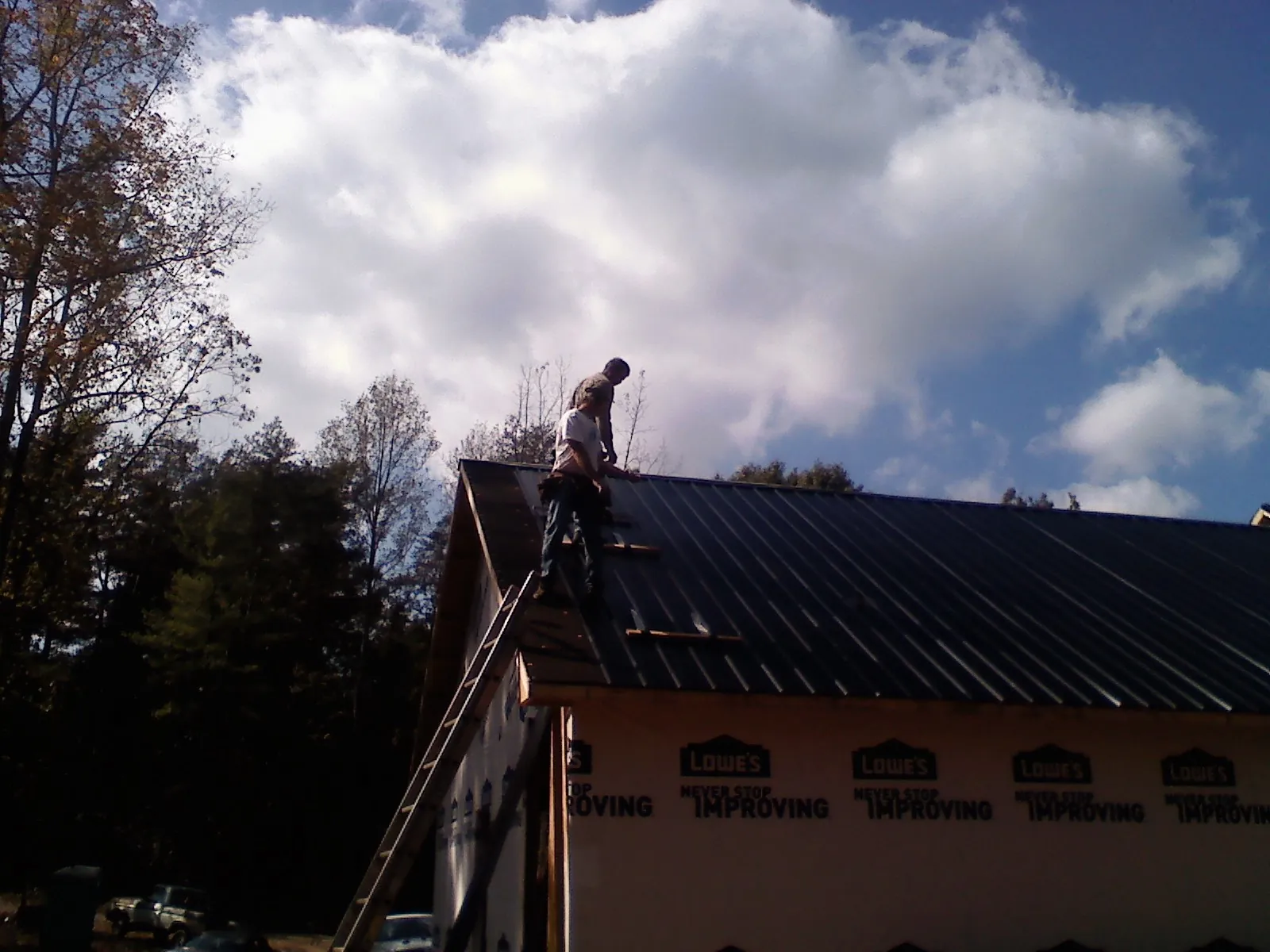 Roofer fastening dark metal panels high against a cloudy sky, from a Roof Inspection job in French Gulch