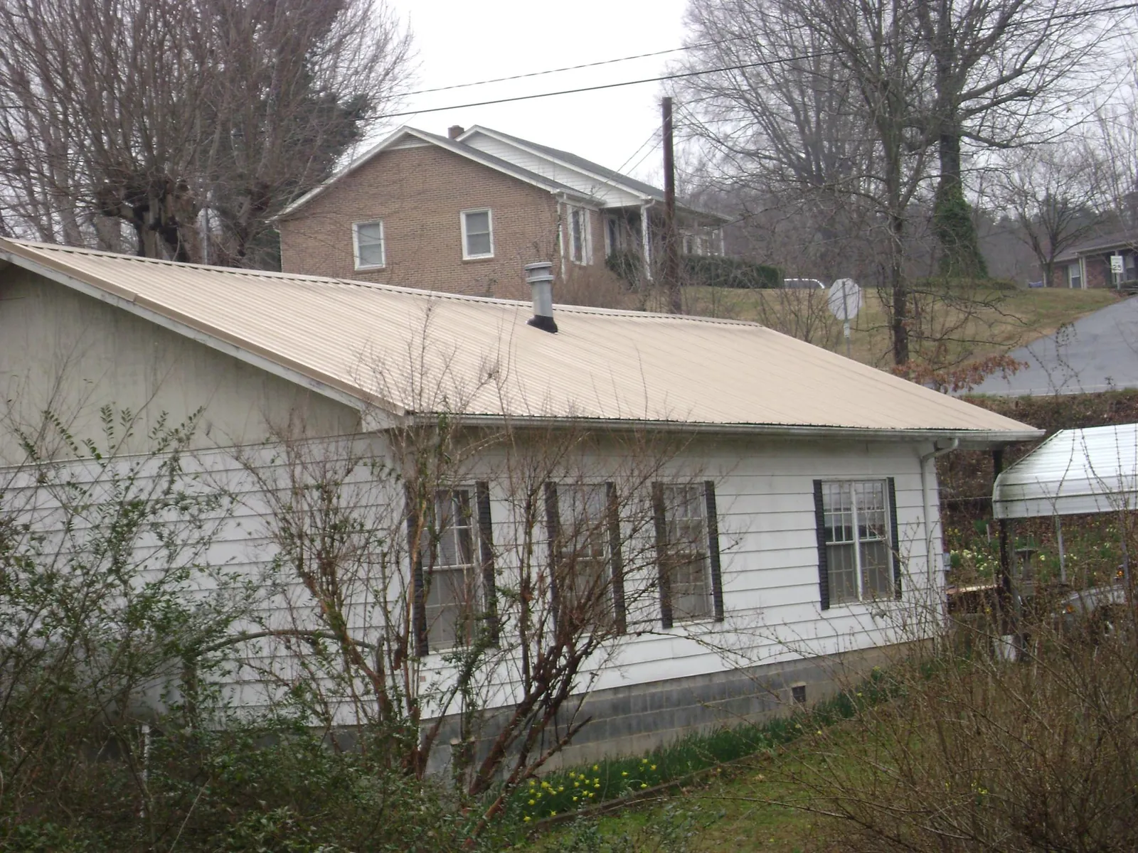 Tan metal roof on a white sided house set into a hillside — Commercial Roofing by Roofing Brothers in French Gulch